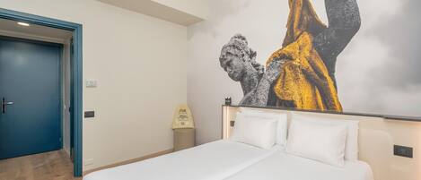 A hotel room with a bed, a blue door, and a wall with a large artwork.