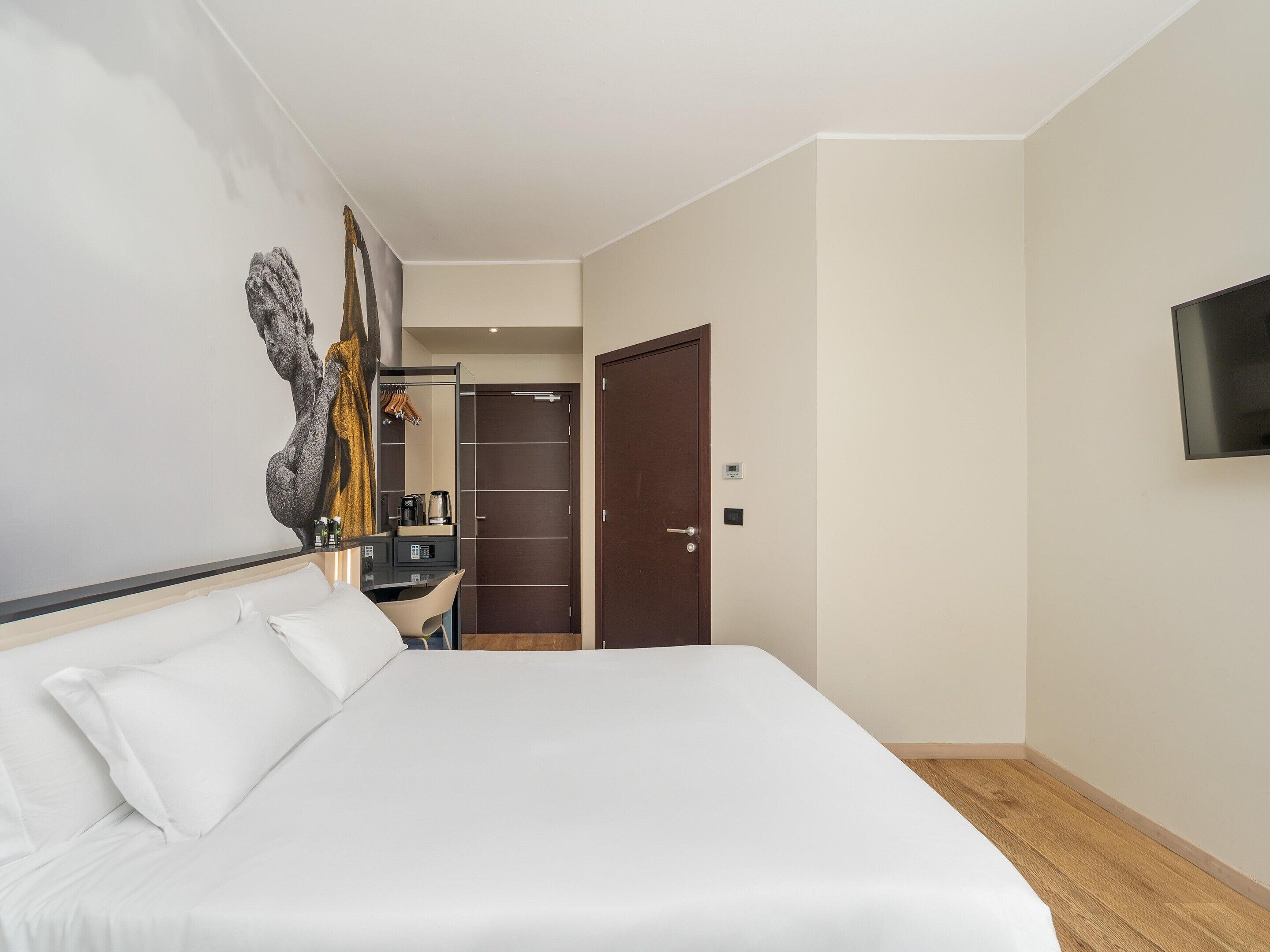 A hotel room with a bed, a desk, a mirror, a wardrobe, and a television.