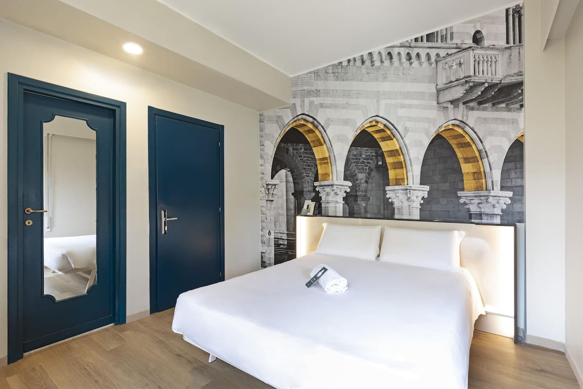 Ein Hotelzimmer mit einem großen Bett, einer dunkelblauen Tür und einem Wandgemälde mit Bögen.