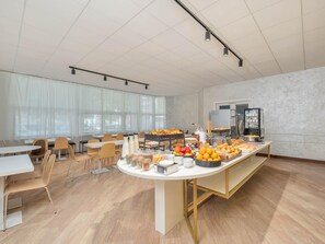 A spacious room with a long table set for breakfast, featuring various food items and beverages. - B&B Hotel Como City Center (Como)