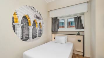 Una habitación de hotel con una cama, una ventana con cortinas, un mural en la pared y una pequeña estantería con una botella.