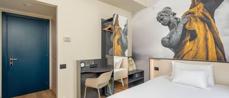A hotel room with a bed, a desk, a chair, a wardrobe, and a large wall mural.