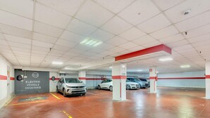 Un garaje con varios niveles, espacios de estacionamiento delimitados y un letrero que indica lugares reservados para vehículos eléctricos.