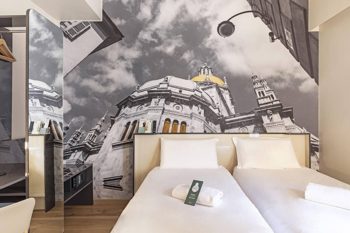 Ein Hotelzimmer mit einem Bett, einem Schreibtisch und einem Wandbild einer Stadtansicht.
