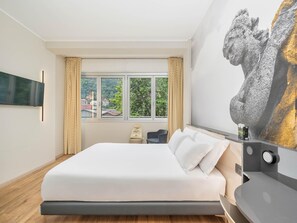 A modern hotel room with a large bed, a flat-screen TV mounted on the wall, a window with curtains, and a painting of a lion's head on the wall. - B&B Hotel Como City Center (Como)
