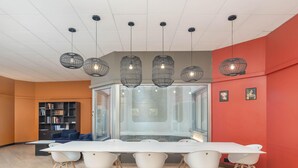 Una sala de reuniones moderna con una mesa larga, sillas blancas y un panel de vidrio.