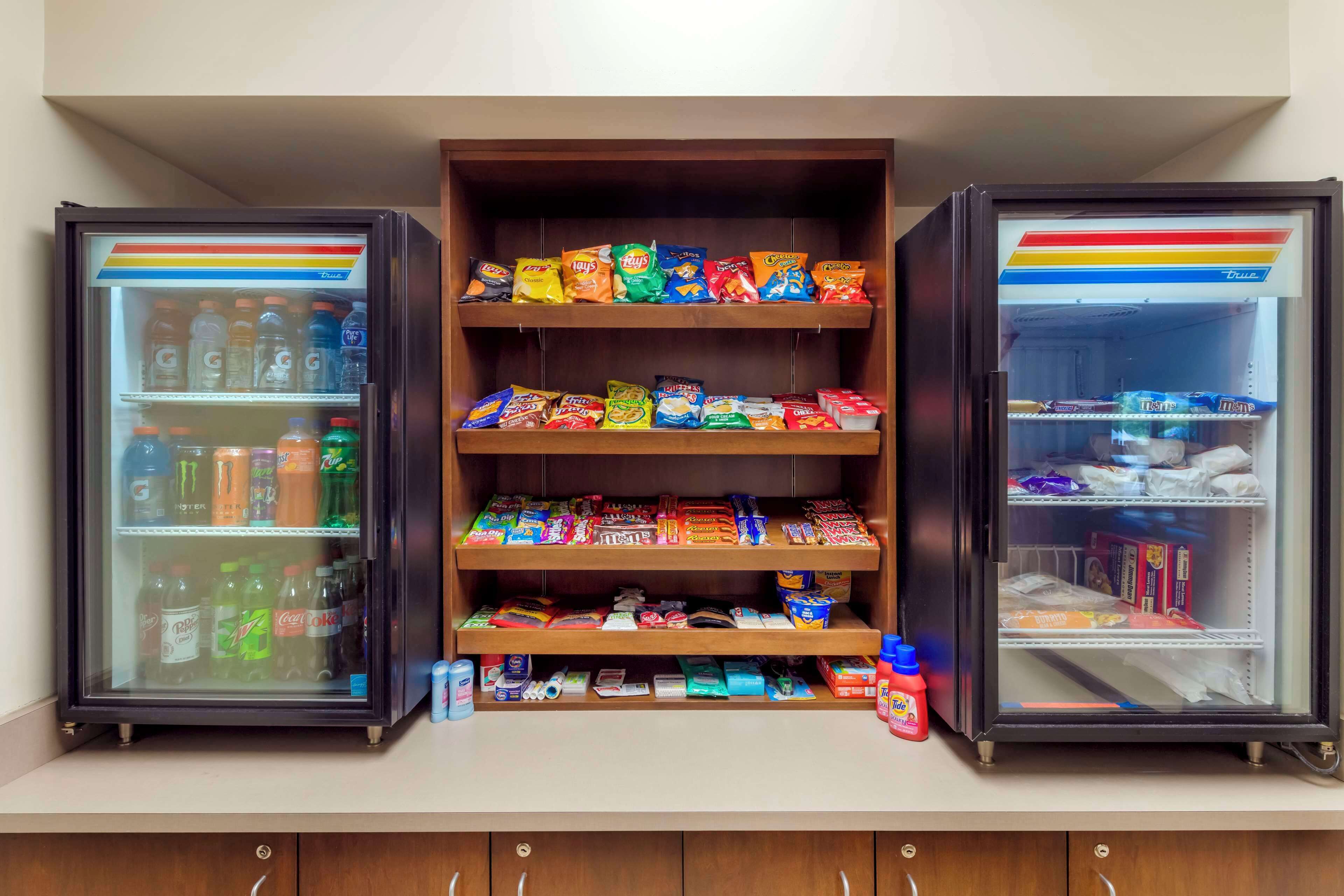 A mini-fridge stocked with various beverages and snacks, including sodas, chips, and candy bars.