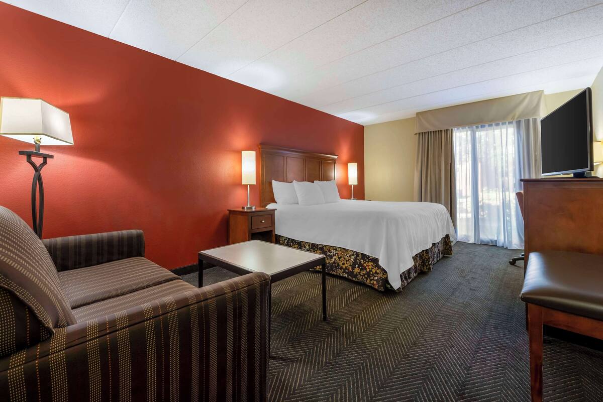 A hotel room with a bed, two bedside tables, a desk, a chair, and a TV.