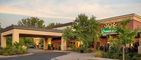 A hotel with a green and gold sign, a covered parking area, and a landscaped entrance.