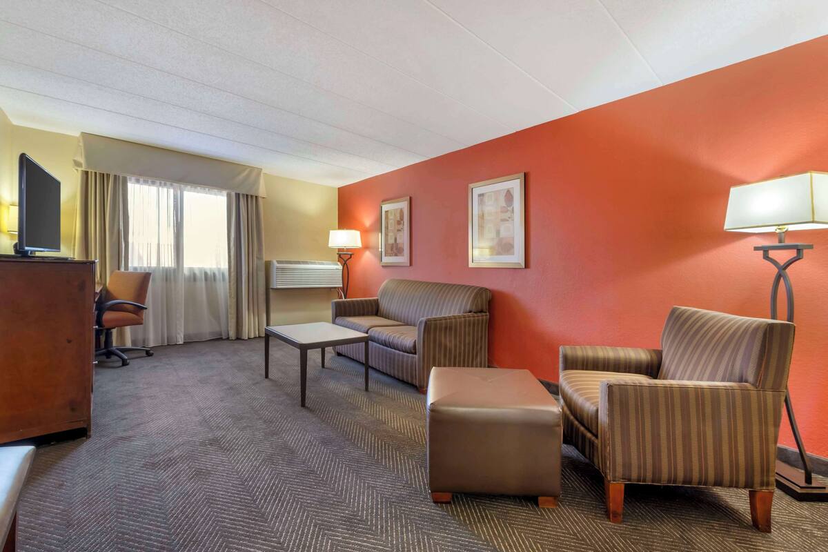 A hotel room with a sofa, armchair, ottoman, desk, and lamp.