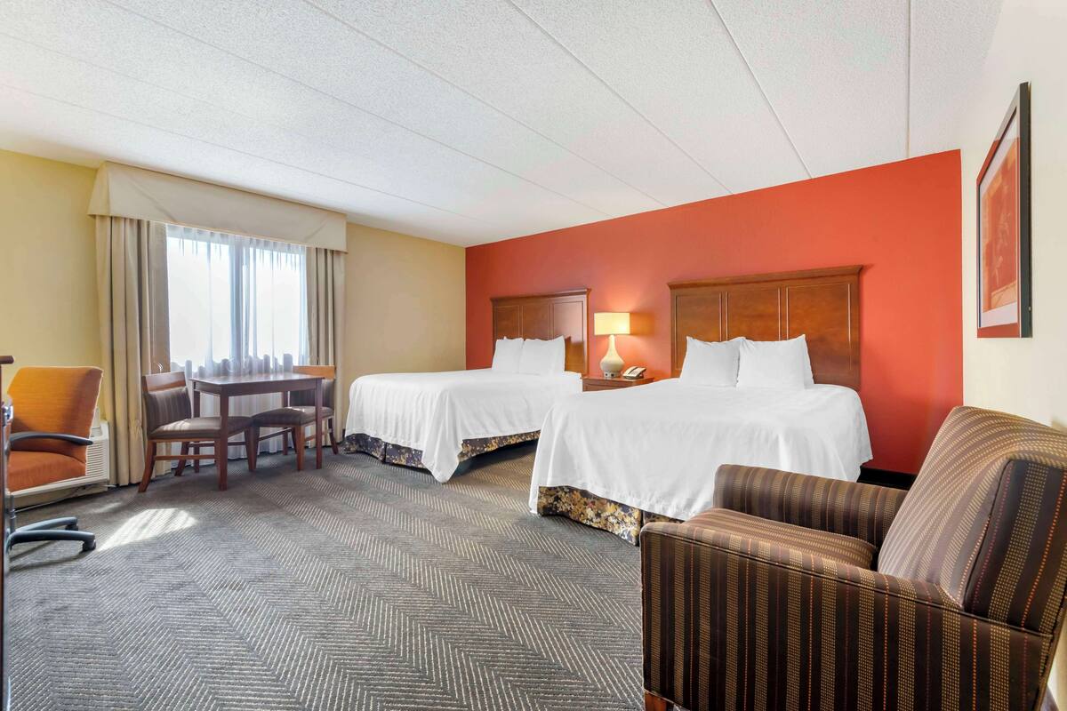 A hotel room with two beds, a desk, and a chair.