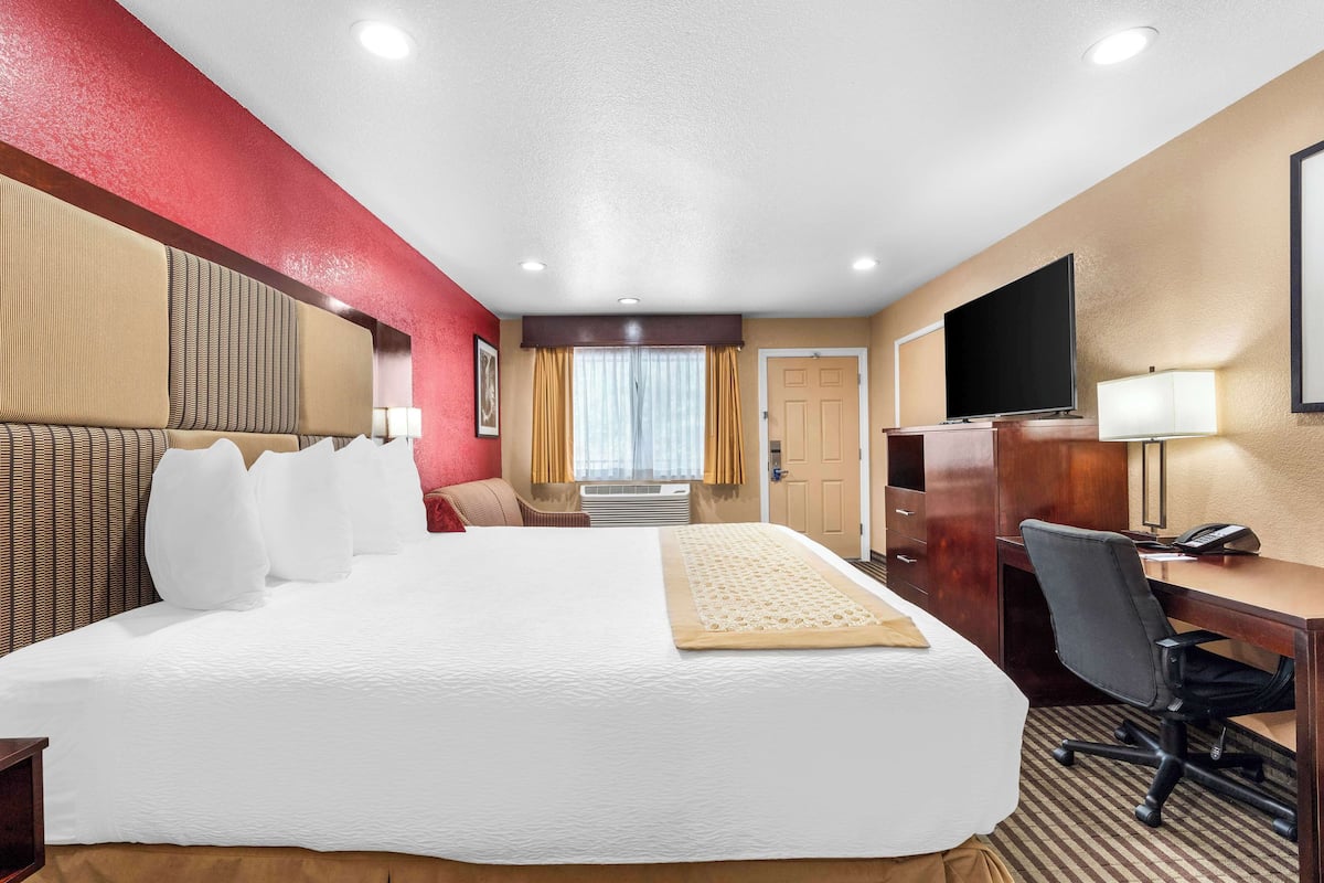 A hotel room with a large bed, a desk, a chair, a television, and a window with curtains.