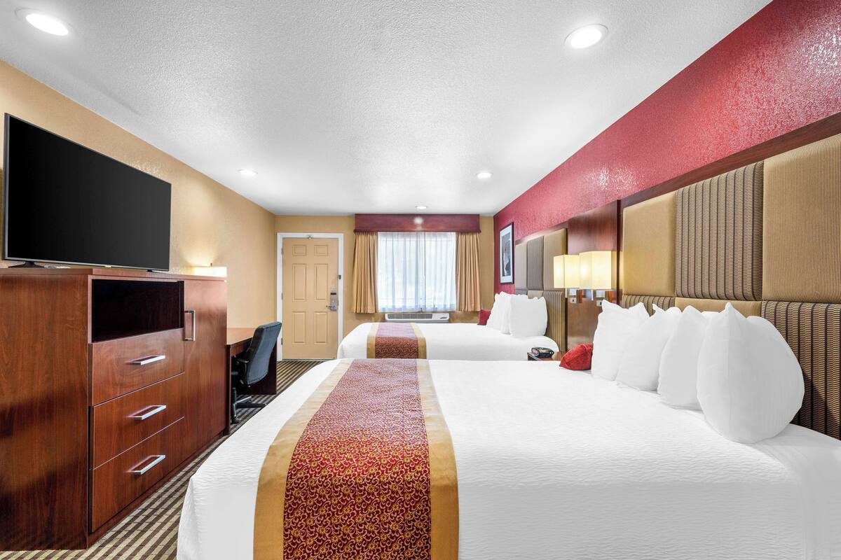 A hotel room with two beds, a TV, a desk, and a large mirror.