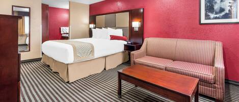 A hotel room with a bed, a sofa, a coffee table, and a large mirror.