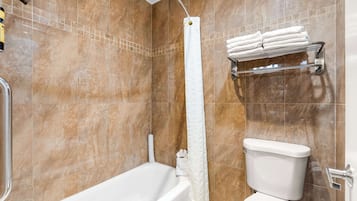 Une salle de bain équipée d’une baignoire, d’un rideau de douche, de toilettes et d’un porte-serviettes.