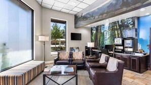 A spacious living area with a large window, comfortable seating, a coffee station, and a mural of a forest scene.