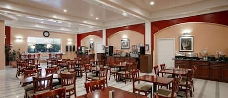 Um restaurante amplo com várias mesas e cadeiras, um balcão com uma máquina de café e um relógio na parede.