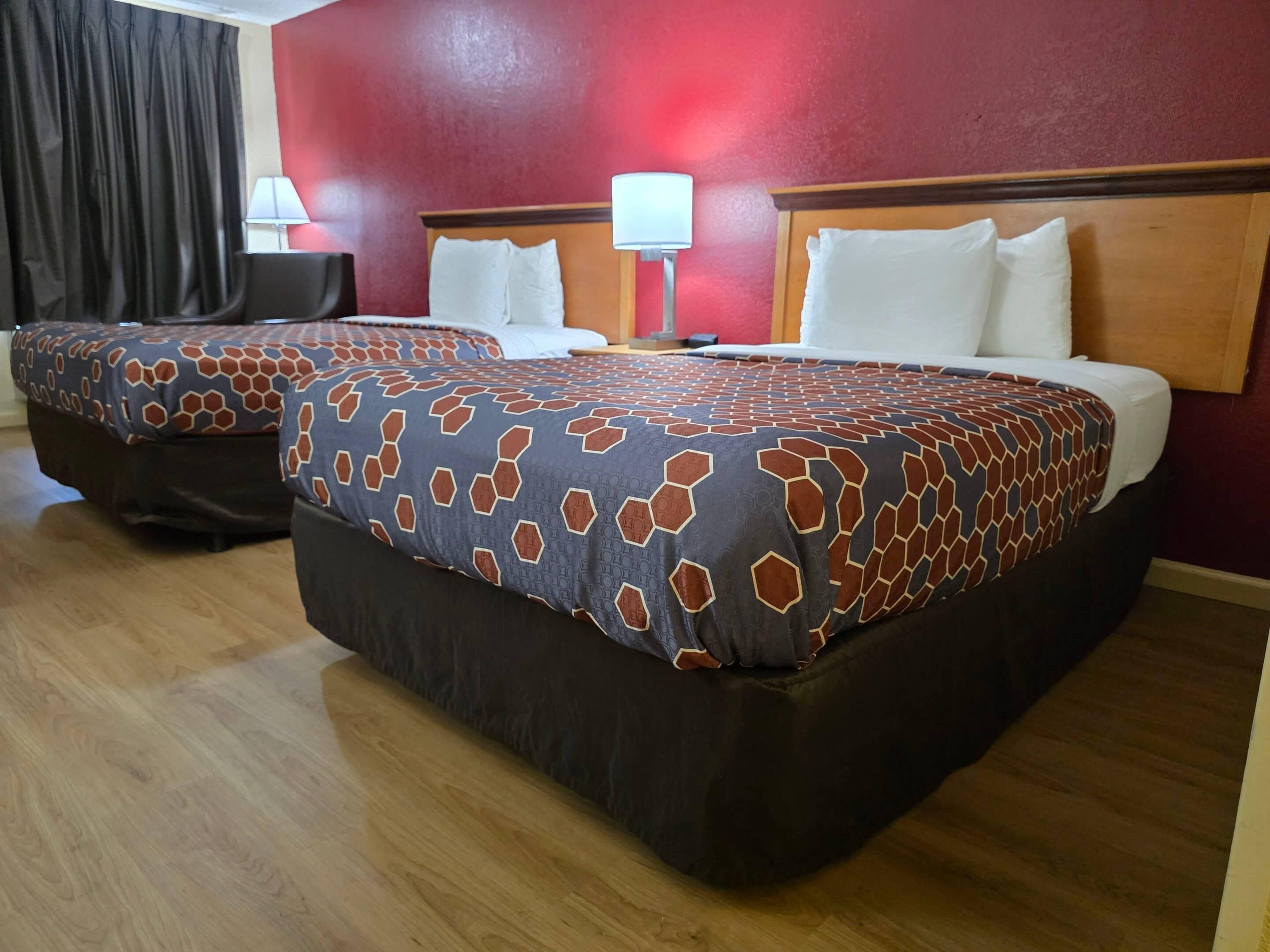 Habitación de hotel con dos camas, una pared roja y suelo de madera.