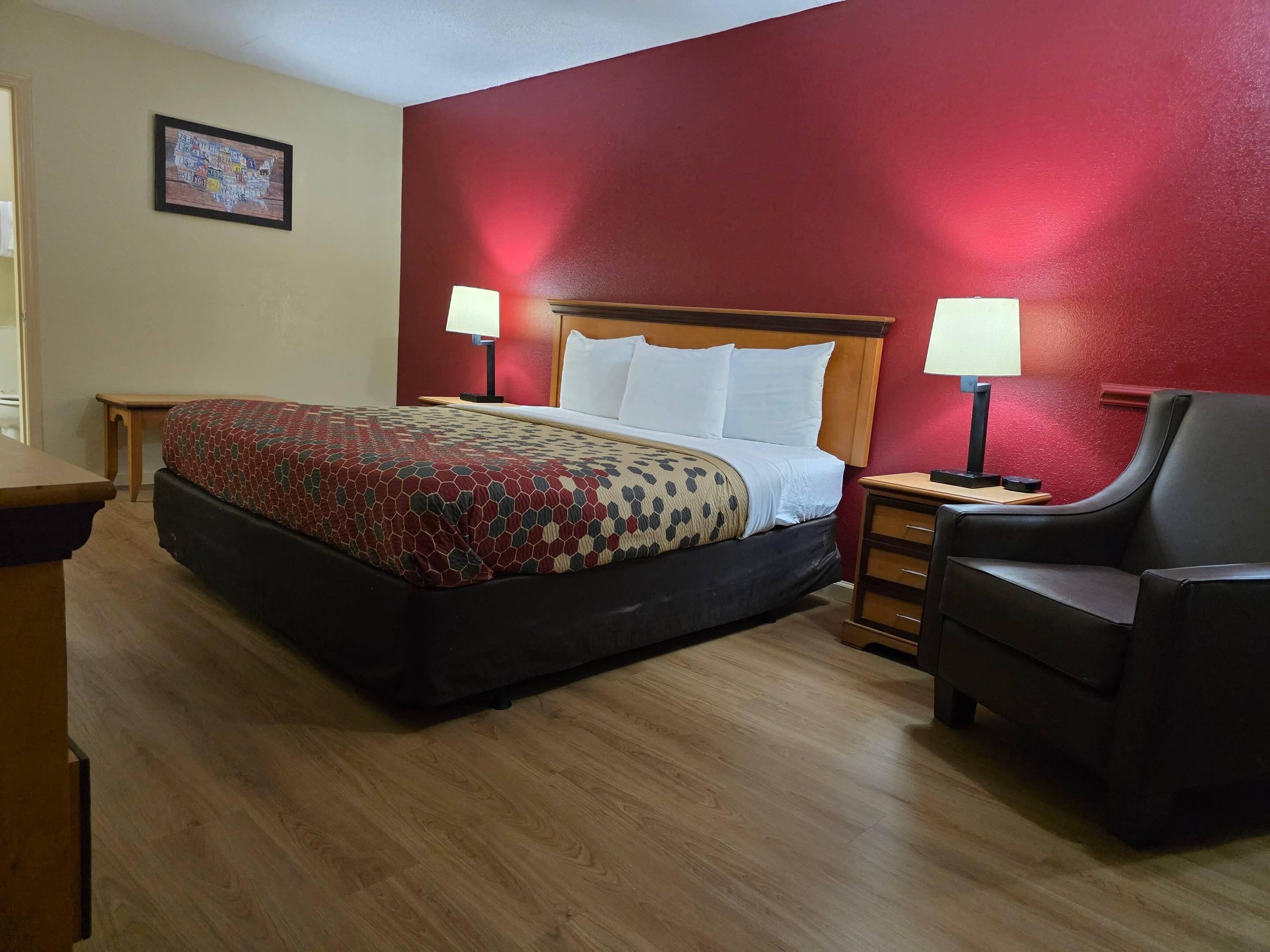 A hotel room with a bed, two bedside lamps, a wooden nightstand, a chair, and a small table.