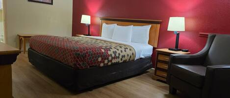 A hotel room with a bed, two bedside lamps, a wooden nightstand, a chair, and a small table.