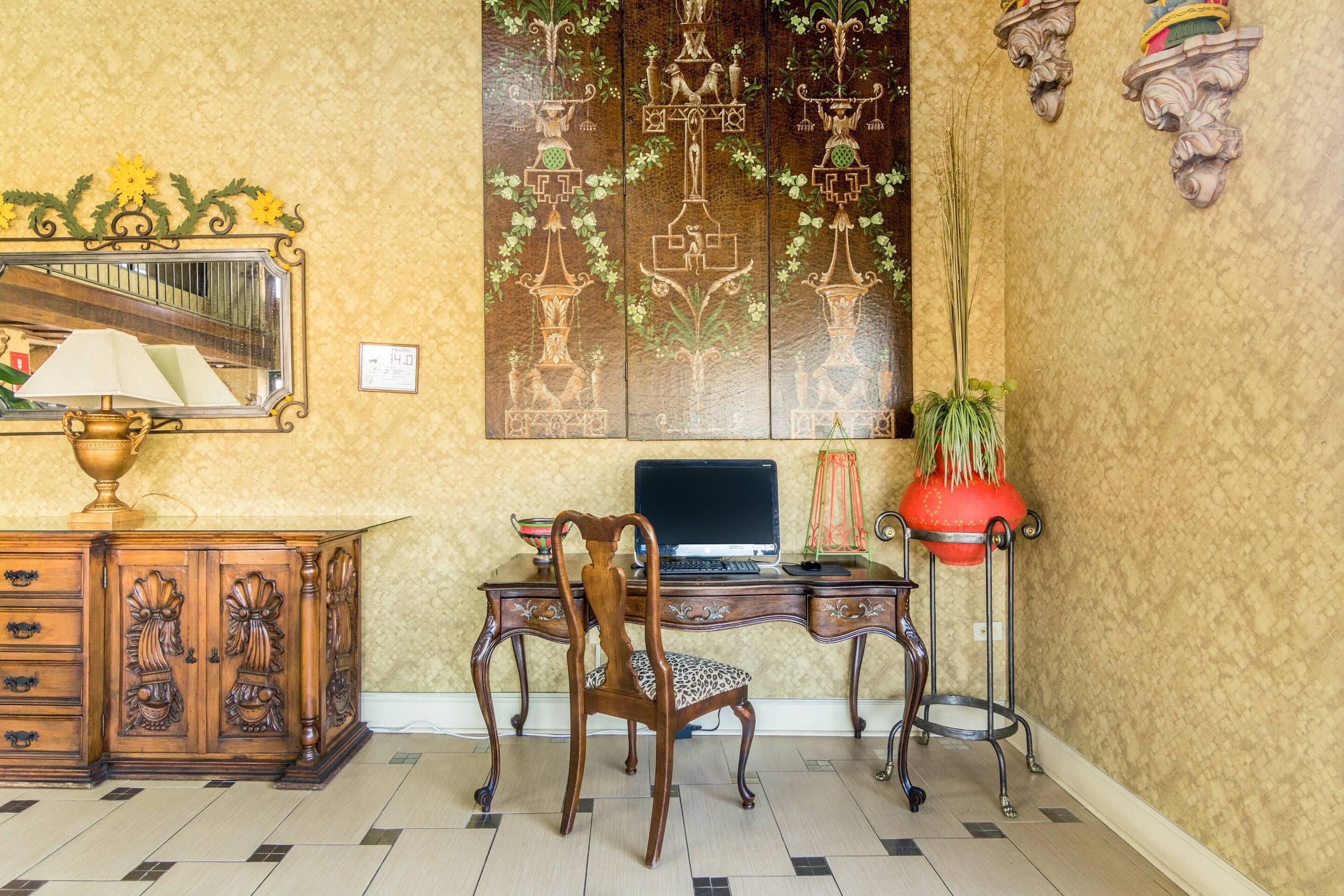A room with a wooden desk, a chair, a computer, a mirror, a potted plant, and a decorative wall panel.