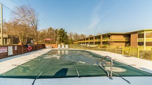 Una piscina con un puesto de socorrista, una cerca amarilla y un edificio de fachada de ladrillo al fondo.