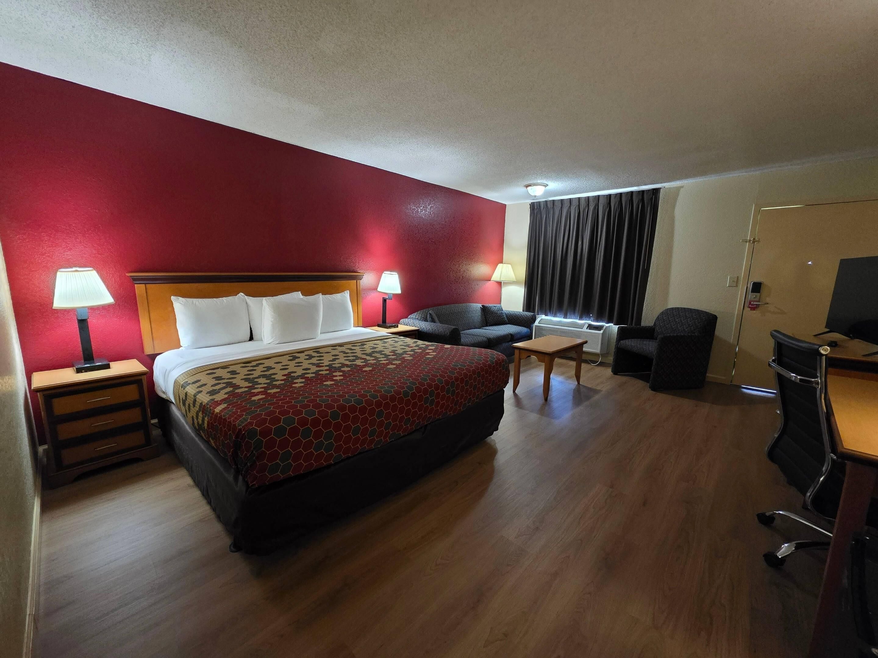 A hotel room with a bed, a desk, a chair, a sofa, and a television.