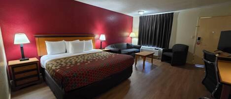 A hotel room with a bed, a desk, a chair, a sofa, and a television.