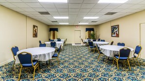 Un salón de conferencias con mesas redondas y sillas azules, piso alfombrado e iluminación en el techo.