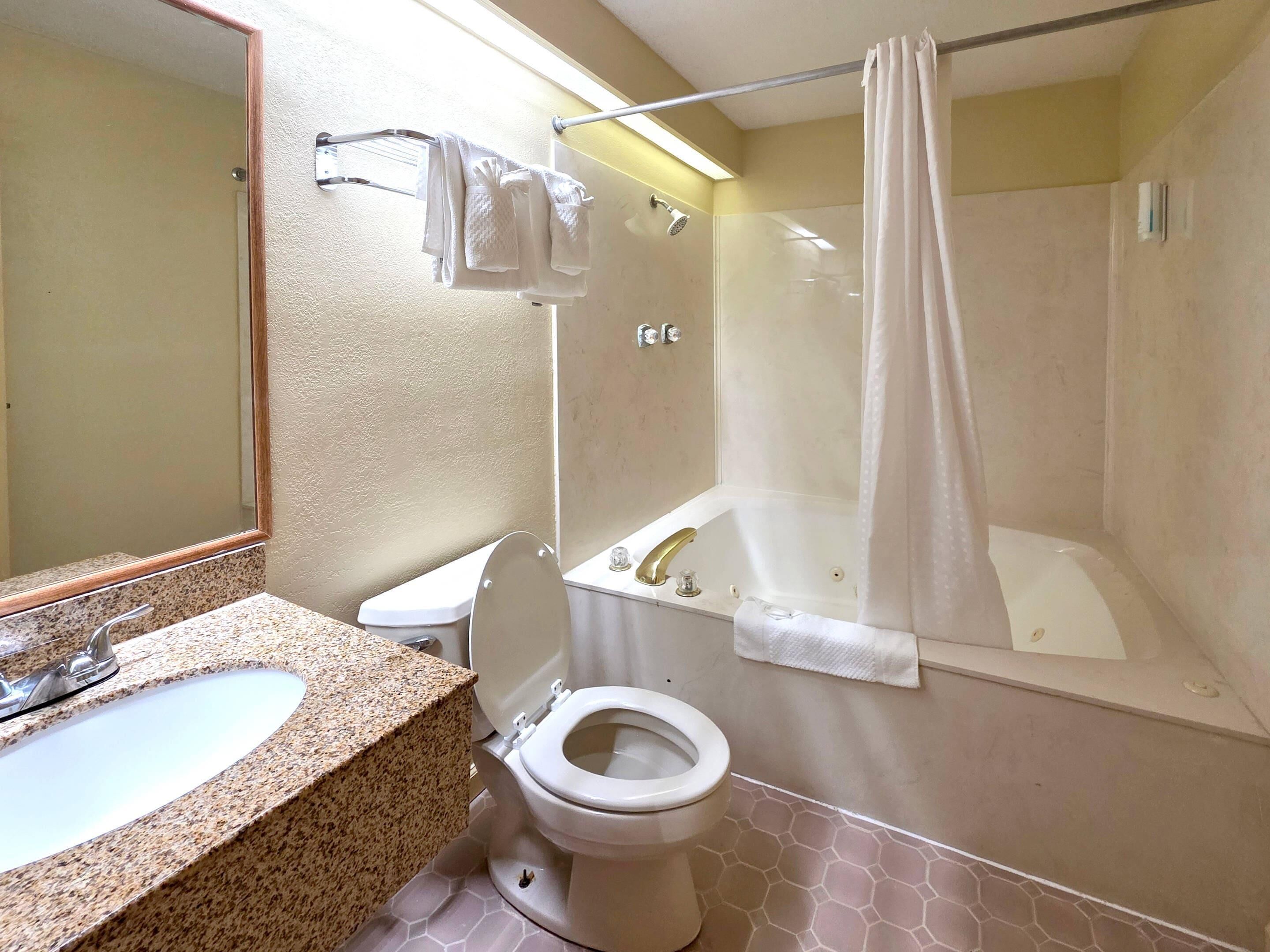 A bathroom with a granite countertop sink, a toilet, a bathtub, and a shower with a curtain.