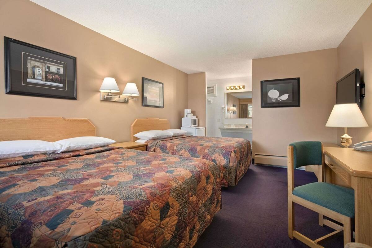 Habitación de hotel con dos camas, un escritorio, una silla y un baño a la vista.