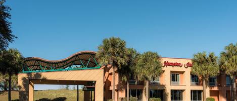 A Hampton Inn hotel with a clear sky, a covered entrance, and palm trees.