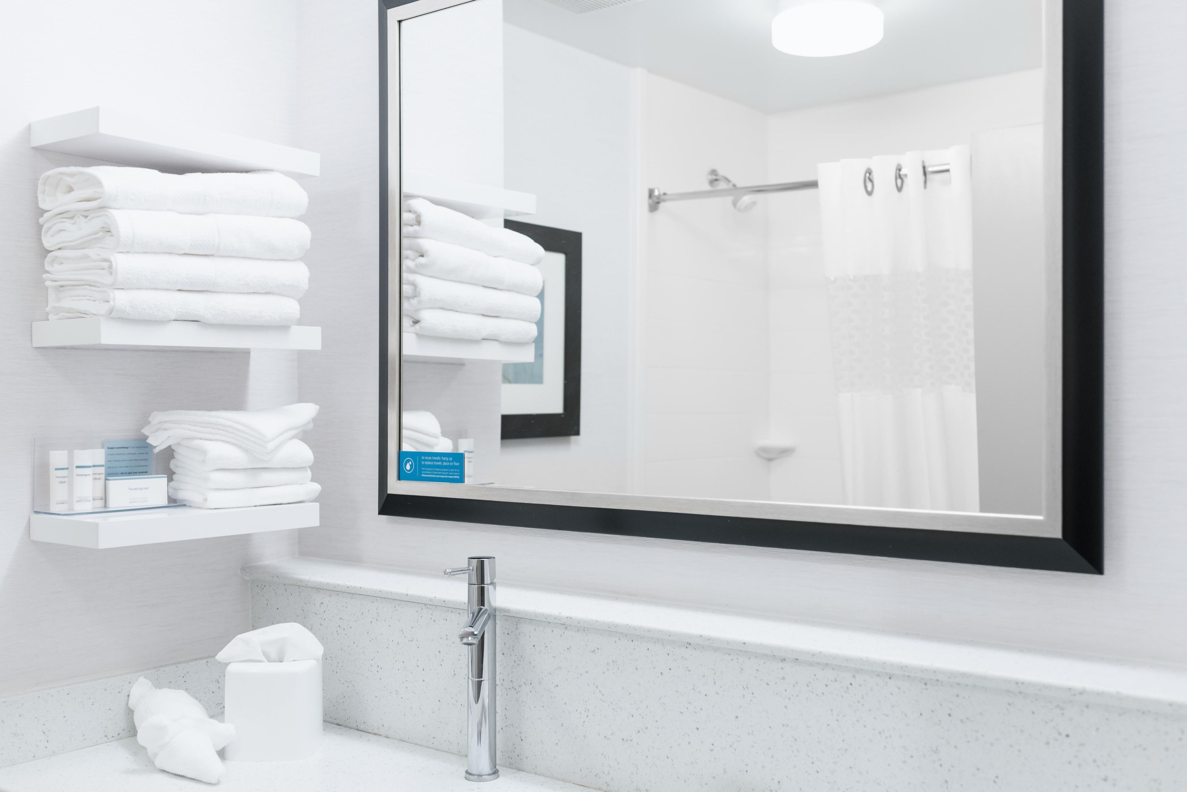 A modern bathroom with a large mirror, a sink, and neatly stacked towels.
