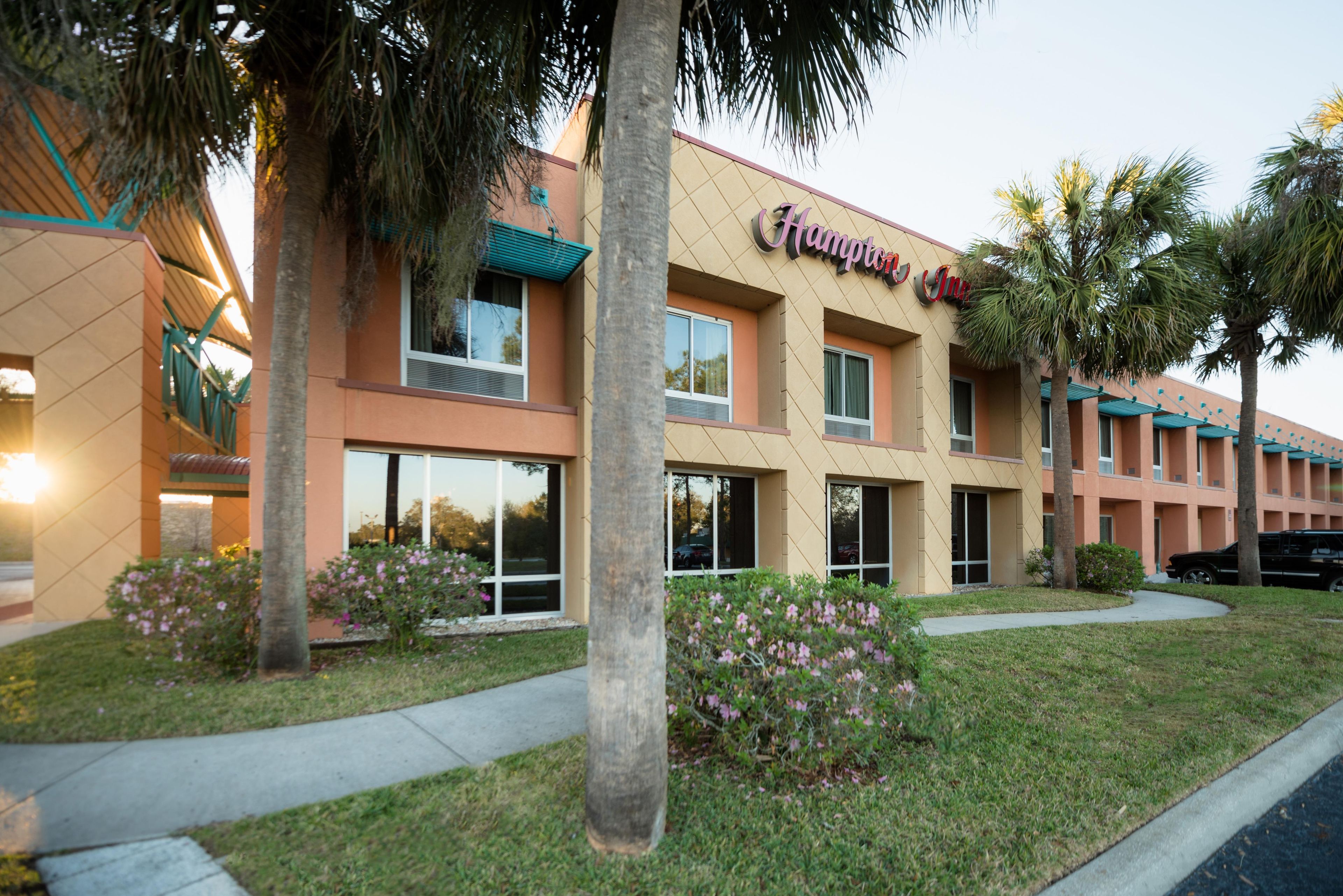Ein Hampton Inn Hotel mit moderner Fassade, zahlreichen Fenstern und einem gepflegten Rasen mit Blumen.