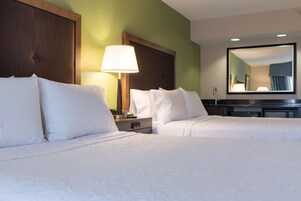 Habitación de hotel con dos camas, una mesita de noche, una lámpara, un espejo y un aparador.