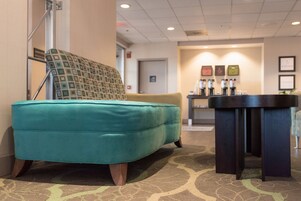 A teal sofa and a dark wooden table in a hotel lobby with a patterned carpet and framed pictures on the wall.