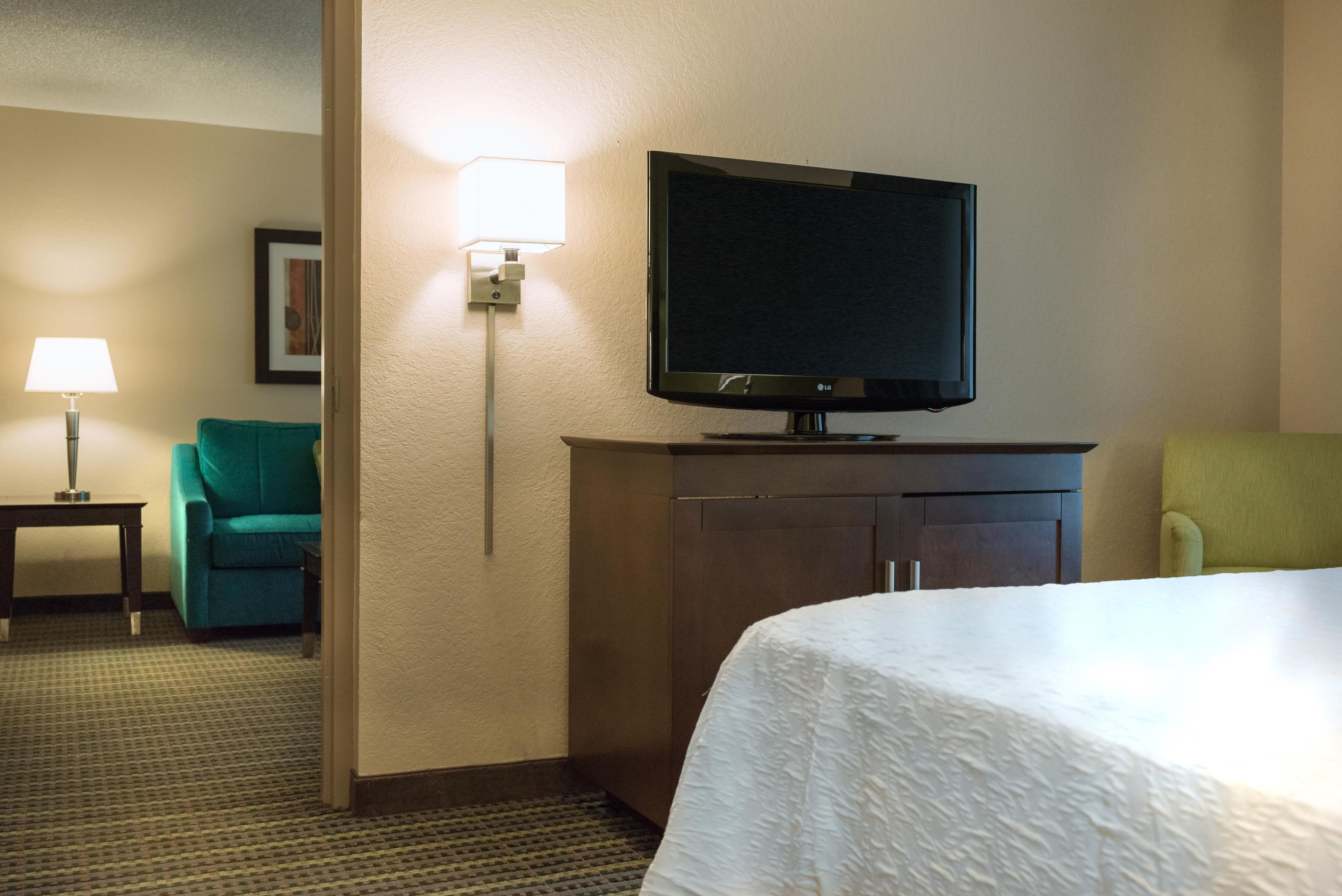 Una habitación de hotel con una cama, un televisor sobre un mueble, un escritorio con una lámpara y dos sillas.