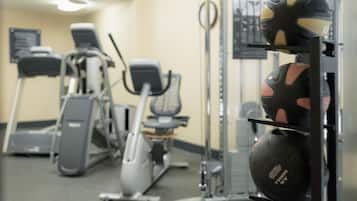 Een fitnessruimte met trainingsapparatuur, waaronder loopbanden, hometrainers en een rek met gewichten en fitnessballen.
