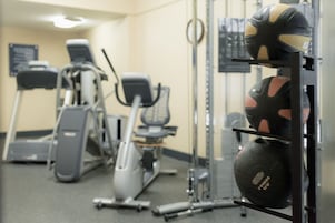 A gym with exercise equipment including treadmills, stationary bikes, and a weight rack with exercise balls.