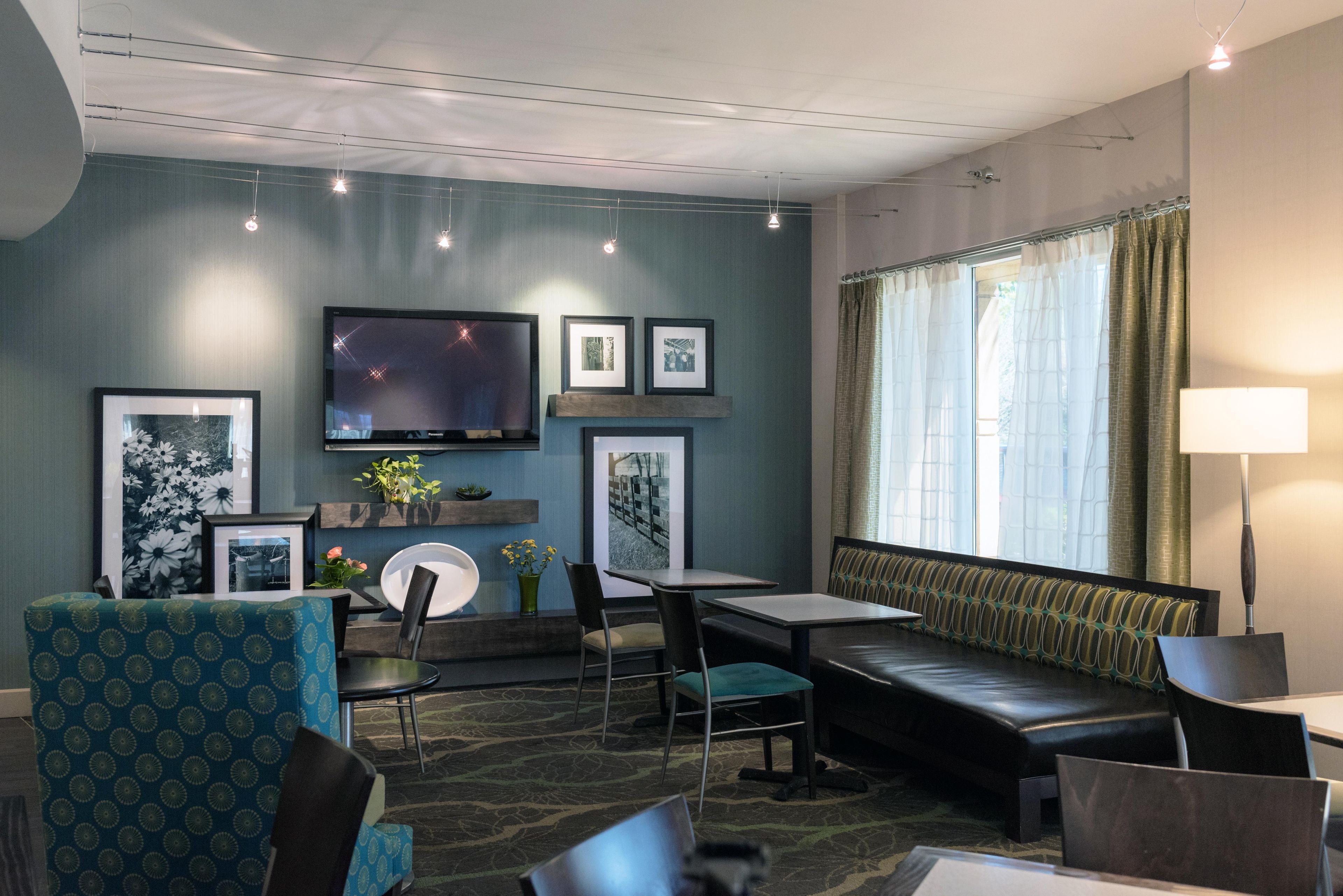 A hotel room with a sofa, chairs, a TV, framed pictures, and a window with curtains.