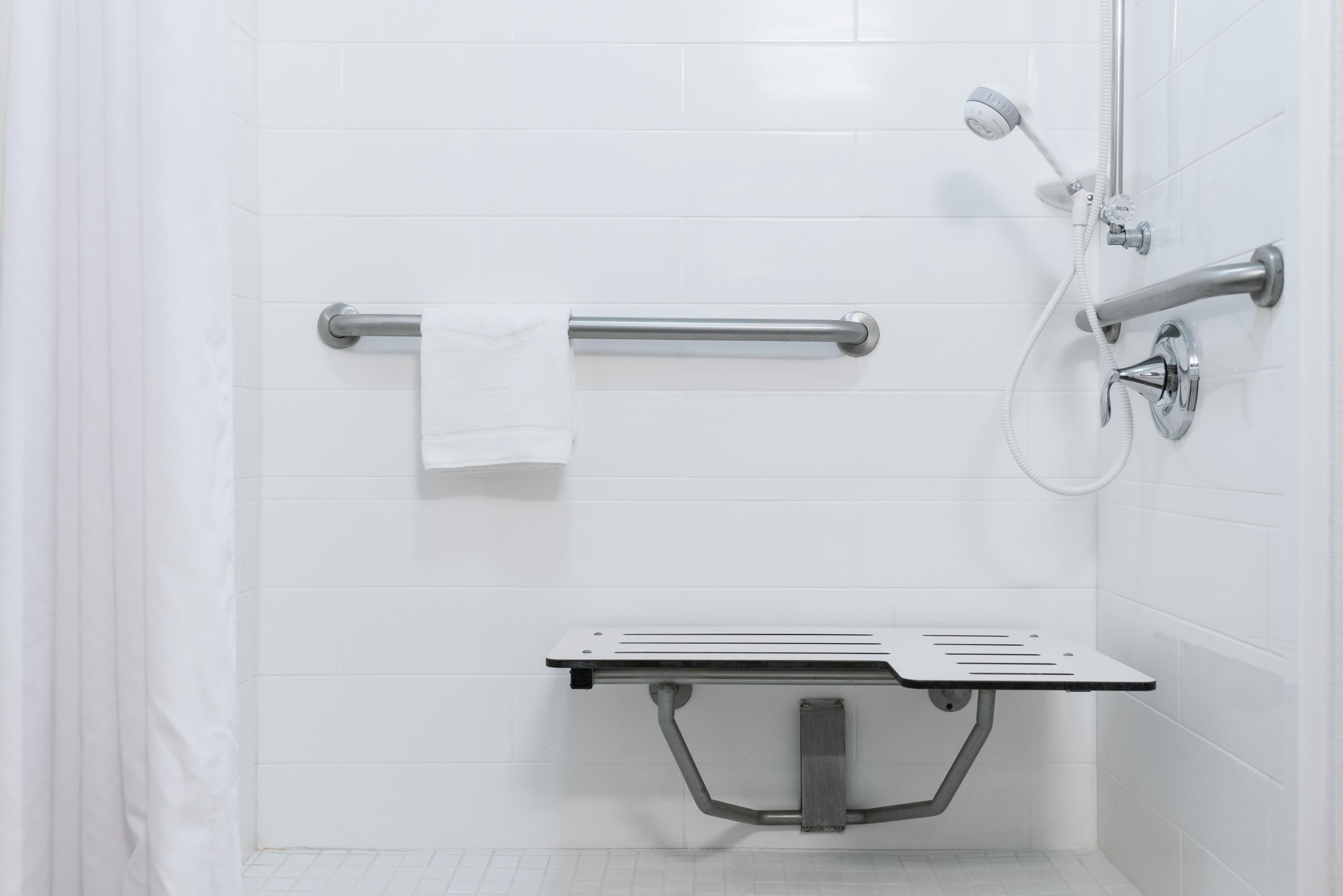 A shower area with a grab bar, a handheld showerhead, and a handheld faucet.