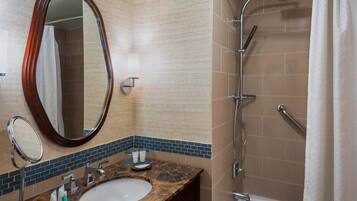A bathroom with a marble sink, a large mirror, a shower with a handheld showerhead, and a towel rack.