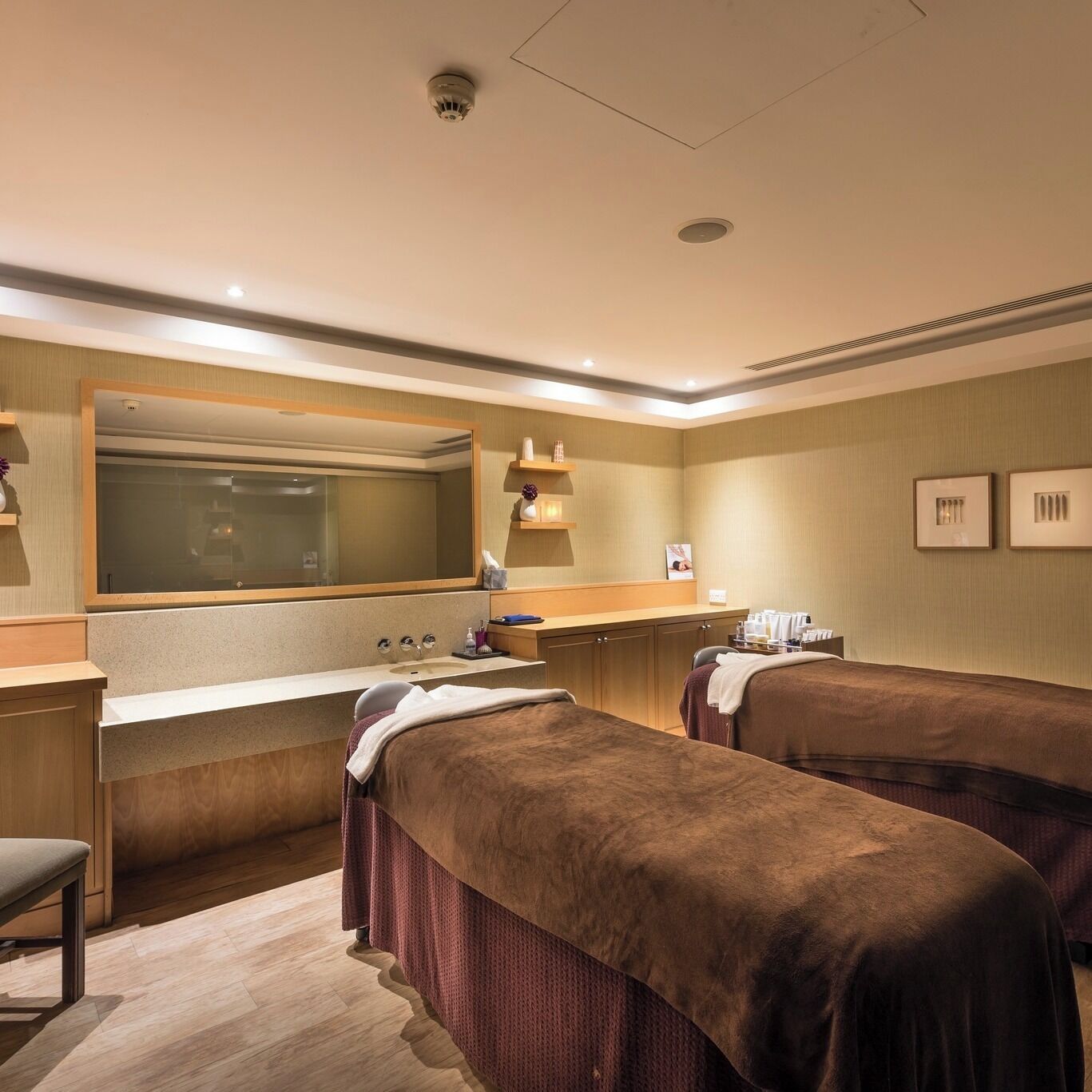 A hotel room with two beds, a large mirror, a vanity with a sink, and a small table with toiletries.
