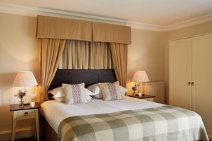 A neatly made bed with a checkered bedspread, two bedside lamps, and a nightstand with a vase of flowers.