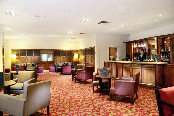 Vestíbulo de hotel con zona de bar, arreglos de asientos y alfombra estampada.