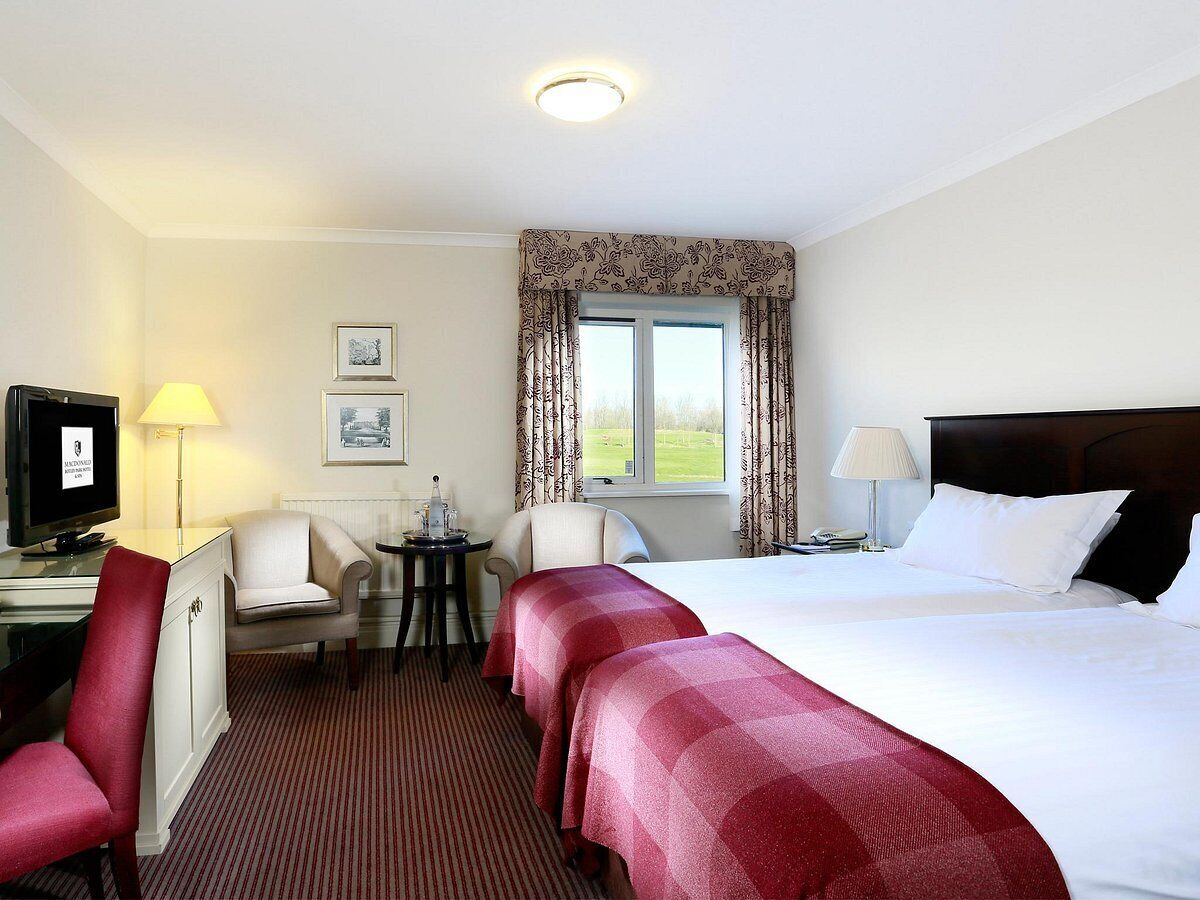 A hotel room with a bed, two bedside tables, a desk with a chair, a television, and a window with curtains.