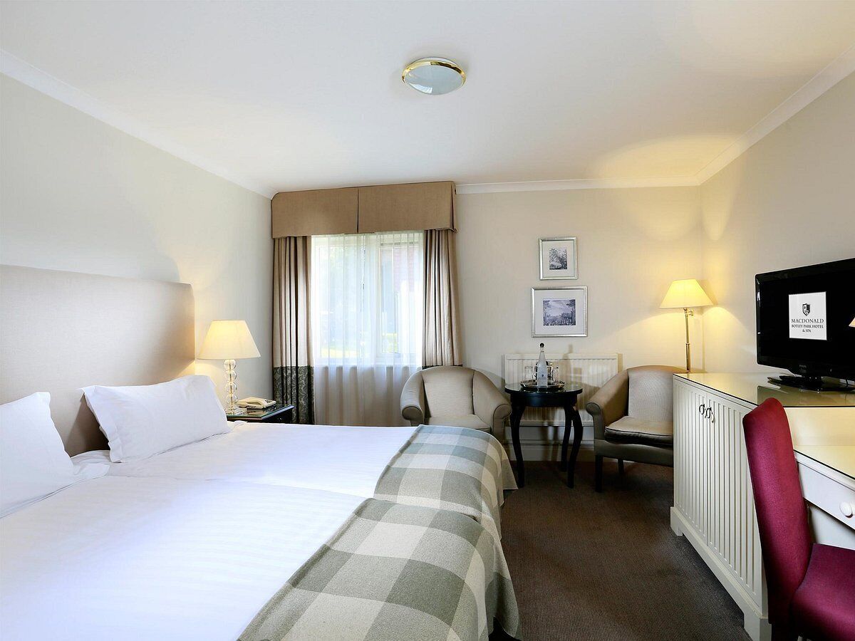 A hotel room with a large bed, two armchairs, a desk with a television, and a window with curtains.