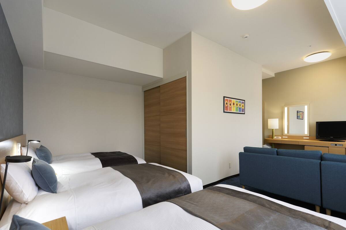 A hotel room with two beds, a desk with a TV, and a seating area.