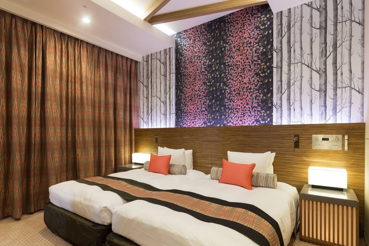 A hotel room with a large bed, two bedside tables, a headboard with a control panel, and a wall with a forest-themed mural.