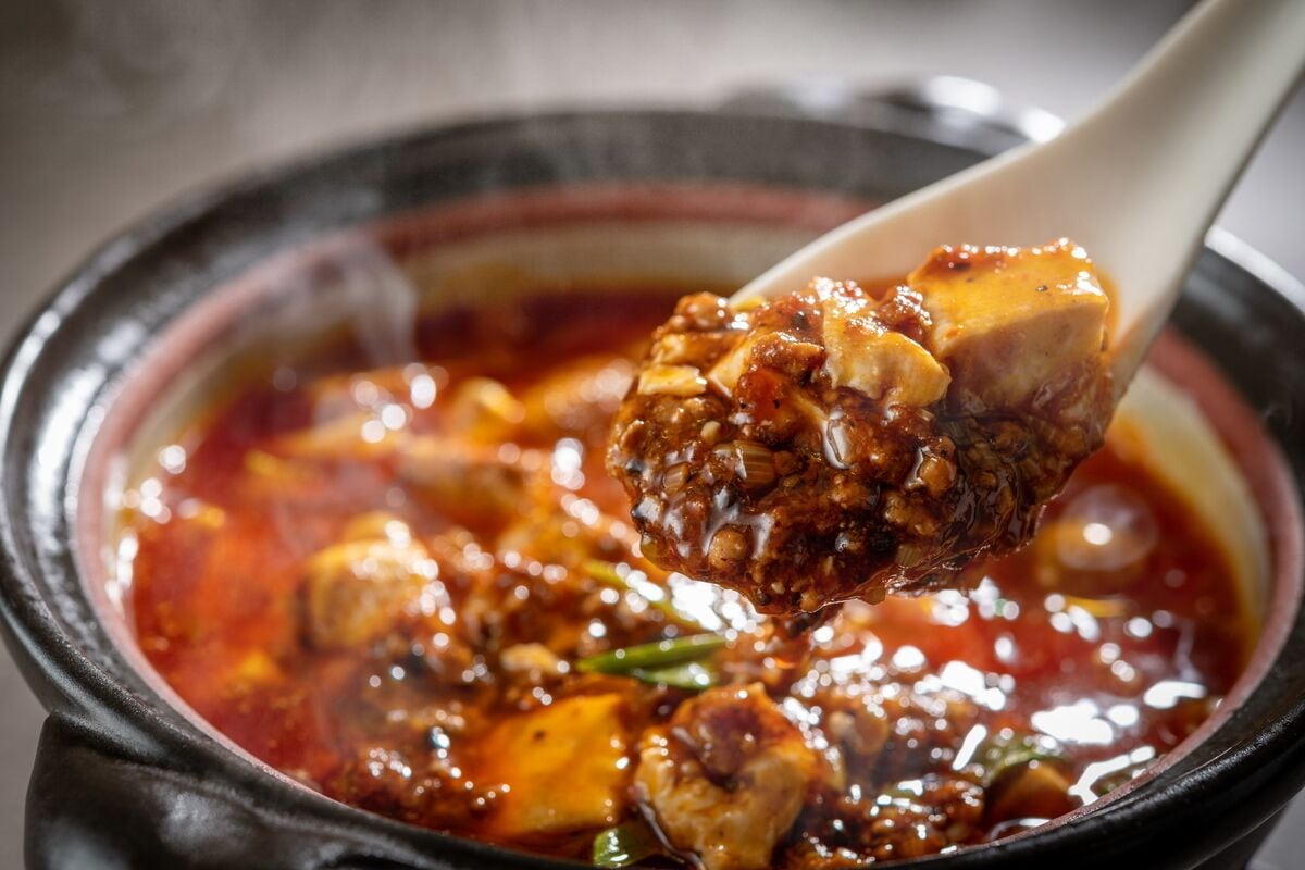A close-up of a bowl of spicy stew with chunks of meat and vegetables, served in a black pot.
